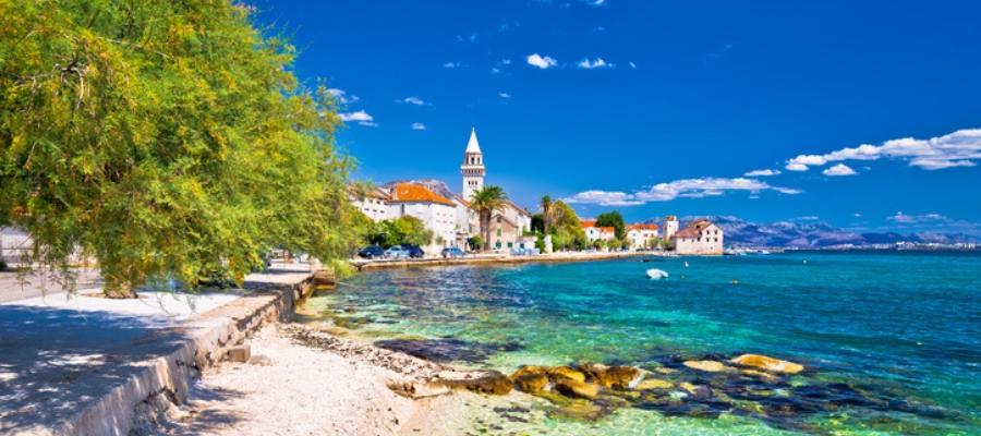 Pemandangan Kroasia di musim panas, dengan pantai berpasir putih, laut biru jernih, dan langit cerah, menciptakan suasana liburan yang menyegarkan dan menenangkan.