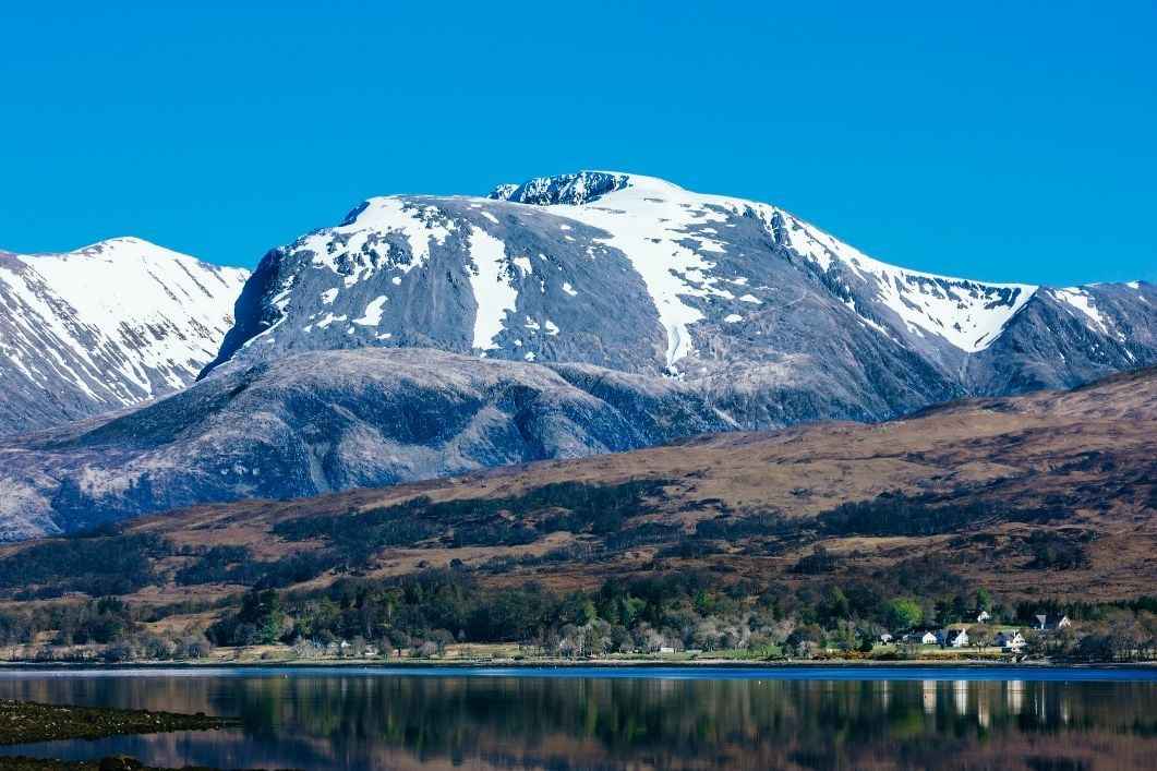 Pemandangan Gunung Ben Nevis dengan langit cerah dan puncaknya tertutup salju, cocok untuk pendakian gunung untuk pemula melalui jalur yang aman dan sering dilalui.