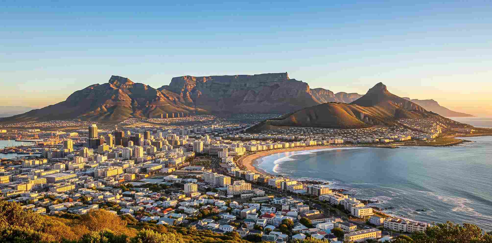 Lanskap Cape Town, Afrika Selatan, menampilkan Table Mountain yang ikonik, cakrawala kota yang semarak, dan garis pantai yang indah, di bawah langit cerah saat matahari terbit. Pemandangan menakjubkan ini adalah salah satu daya tarik utama untuk wisata di Afrika Selatan.